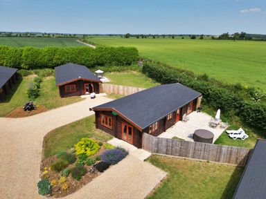 Aerial view of two wooden lodges with outdoor seating and garden surrounded by fields at Oak Lodge in Greetham Rutland