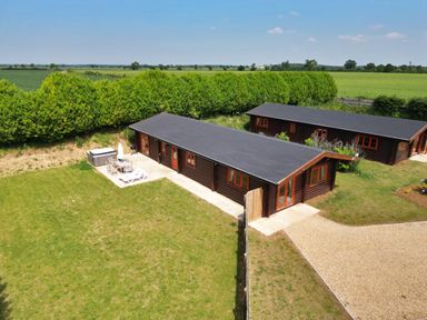 Two wooden lodges with patios and outdoor furniture in a green field at Oak Lodge in Greetham Rutland