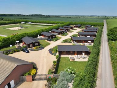 An aerial view of wooden lodges with patios and greenery along a gravel road at Oak Lodge in Greetham Rutland