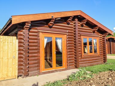 A wooden log cabin with glass double doors and a window at Holly Lodge in Greetham Rutland