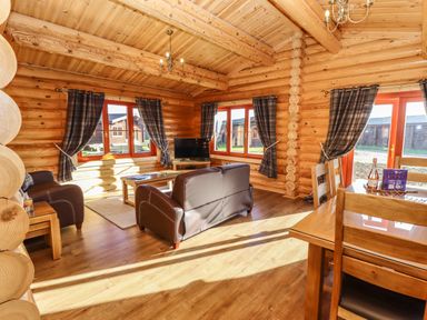 A living room with wooden furniture and a television in a log cabin at Holly Lodge in Greetham Rutland