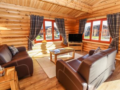 A living room with brown leather sofas a wooden coffee table a television and plaid curtains at Holly Lodge in Greetham Rutland