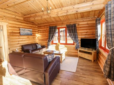 A living room with brown leather sofas a wooden coffee table a television on a wooden stand and plaid curtains at Holly Lodge in Greetham Rutland