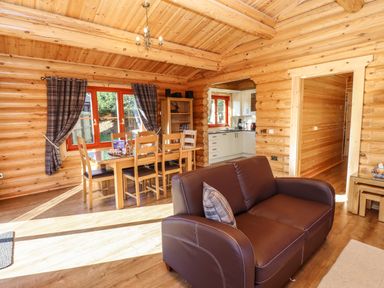 A wooden interior with a brown sofa a dining table with chairs and a kitchen visible through an open doorway at Holly Lodge in Greetham Rutland