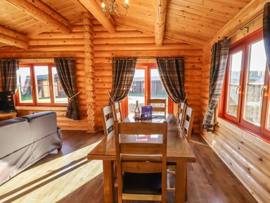 A dining area with a wooden table and six chairs in a wooden log cabin with windows and a glass door at Holly Lodge in Greetham Rutland
