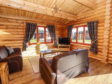A living room with leather sofas a coffee table a television and windows with plaid curtains at Holly Lodge in Greetham Rutland