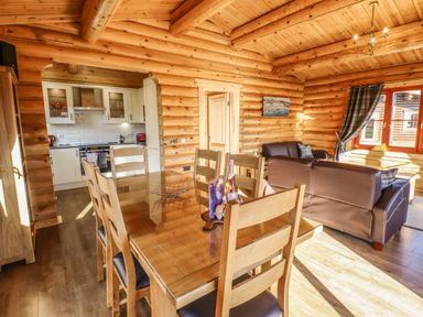 A dining area with wooden table and chairs opening to a kitchen and living room in a wooden log cabin at Holly Lodge in Greetham Rutland