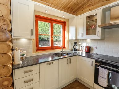 A kitchen with white cabinets black countertop and a red window frame at Holly Lodge in Greetham Rutland