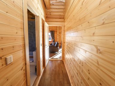 A wooden hallway with a bathroom door on the left and a view of a living room with chairs and a window at Holly Lodge in Greetham Rutland