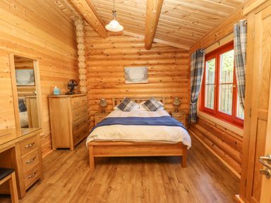 A bedroom with a wooden bed dresser two nightstands two lamps a window with curtains and wooden walls at Holly Lodge in Greetham Rutland