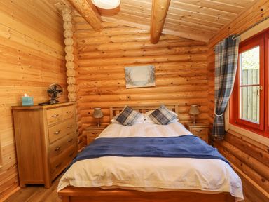 A bedroom with a double bed two bedside tables with lamps a chest of drawers and a window with plaid curtains at Holly Lodge in Greetham Rutland
