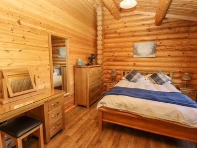 A bedroom with a wooden bed blue throw pillows wooden dressers and a dressing table at Holly Lodge Greetham Rutland