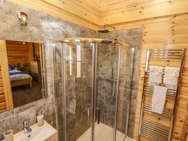 A bathroom with a glass shower enclosure a sink with soap dispenser and toothbrush holder and a towel rack with towels at Holly Lodge Greetham Rutland