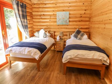 A bedroom with two single beds a nightstand a lamp and a window with curtains at Holly Lodge in Greetham Rutland