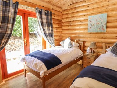 A bedroom with two single beds and wooden walls and floor with a nightstand and window at Holly Lodge in Greetham Rutland