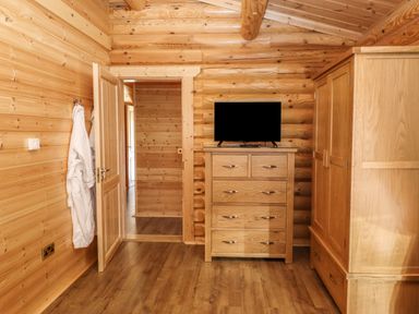 A wooden room with a chest of drawers, a wardrobe, a door, a wall hook with bathrobes, and a television on the chest of drawers at Holly Lodge in Greetham, Rutland