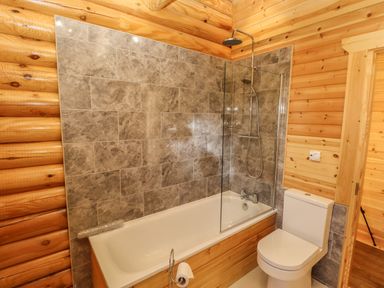 A bathroom with a bathtub shower combination and a toilet in a wooden room at Holly Lodge in Greetham Rutland