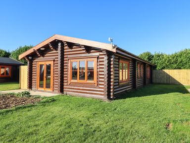 A log cabin with multiple windows and a glass door on a grassy lawn at Holly Lodge in Greetham Rutland