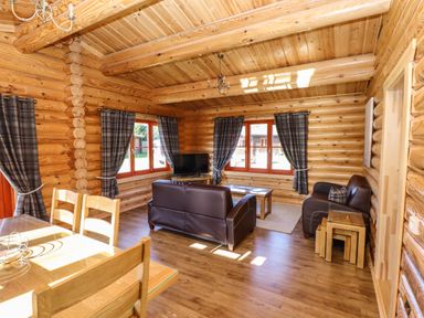 A living room with wooden walls and ceiling brown leather sofas wooden dining table and chairs and windows with plaid curtains at Pine Lodge in Greetham Rutland