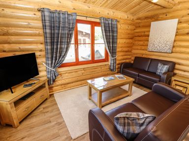 A living room with leather sofas a wooden coffee table a television on a wooden stand and plaid curtains at Pine Lodge in Greetham Rutland