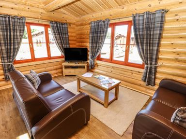 A living room with brown leather sofas a wooden coffee table a television and large windows with plaid curtains at Pine Lodge Greetham Rutland