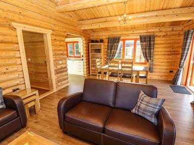 A living room with brown leather sofas and wooden dining table in a log cabin at Pine Lodge in Greetham Rutland
