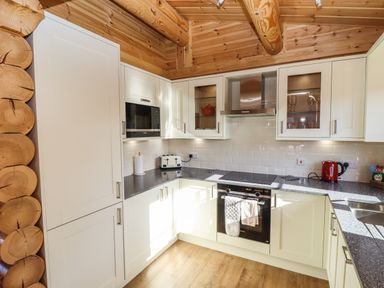 A kitchen with white cabinets black countertop wooden ceiling and wooden floor at Pine Lodge in Greetham Rutland