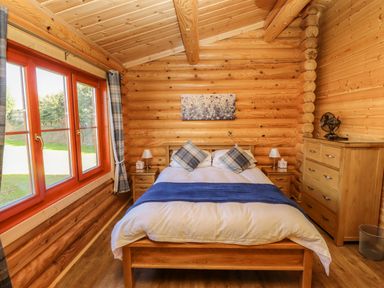 A bedroom with a wooden bed a blue runner two bedside tables with lamps a wooden dresser and large windows at Pine Lodge in Greetham Rutland