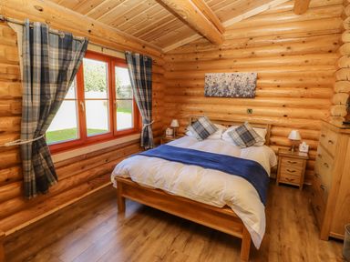 A bedroom with a bed two bedside tables a chest of drawers and a window with curtains at Pine Lodge in Greetham Rutland