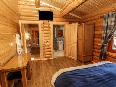 A wooden bedroom with a bed a wardrobe a desk and a doorway leading to a bathroom at Pine Lodge in Greetham Rutland