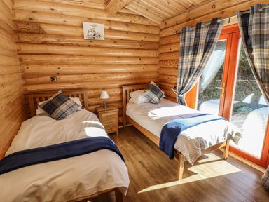 A bedroom with two single beds a nightstand and window with curtains at Pine Lodge in Greetham Rutland