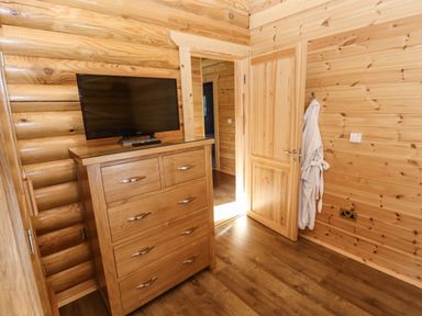 A wooden chest of drawers with a television on top and a wooden door with a bathrobe hanging on a hook in a wooden room at Pine Lodge in Greetham Rutland