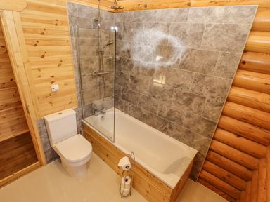 A bathroom with a bathtub with shower and a toilet at Pine Lodge in Greetham Rutland