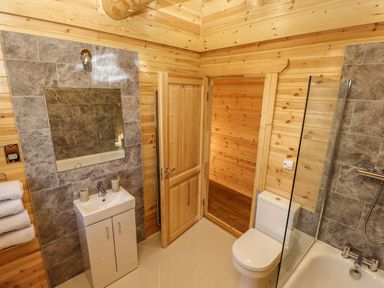 A bathroom with a sink cabinet mirror toilet and bathtub with glass screen at Pine Lodge in Greetham Rutland