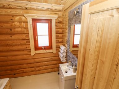 A bathroom with wooden walls a window a sink with towels and toiletries at Pine Lodge in Greetham Rutland