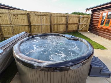 An outdoor hot tub with bubbling water next to a wooden cabin and enclosed by a wooden fence at Pine Lodge in Greetham Rutland