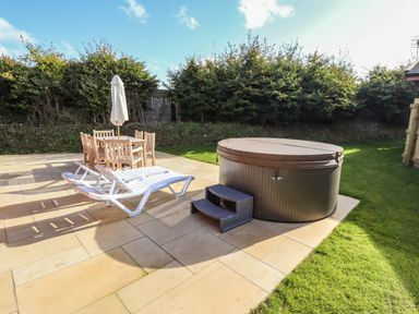 A patio with white lounge chairs a wooden table with parasol and a covered hot tub at Pine Lodge in Greetham Rutland