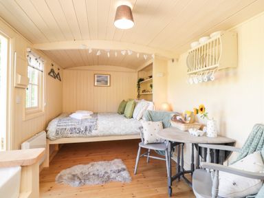 A small room with a bed, two chairs, a small table with a basket of food, and a wall-mounted plate rack at The Shepherds Hut at Marley in Marley near Barham Kent