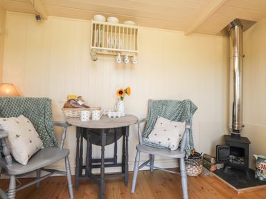 A small dining area with two chairs a round table flowers a basket and a wood stove at The Shepherds Hut at Marley near Barham Kent