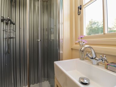 A bathroom with a metal shower enclosure and a sink with a faucet and flowers on the windowsill at The Shepherds Hut at Marley Marley near Barham Kent
