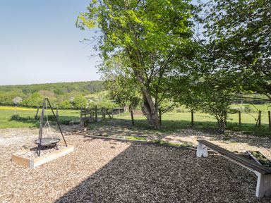 An outdoor area with a fire pit, tree, wooden bench, and fenced grassy fields at The Shepherds Hut at Marley near Barham Kent