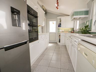 A galley kitchen with white cabinets green tiled backsplash and stainless steel fridge at Robin Hill in Duporth near St Austell