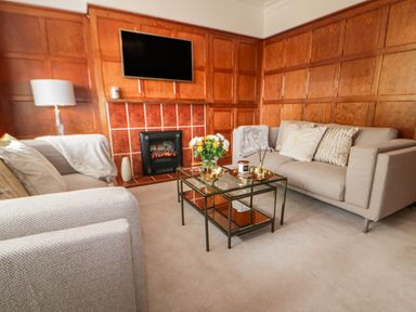 A living room with two sofas a glass coffee table flowers and a television on wooden paneled walls at Robin Hill in Duporth near St Austell