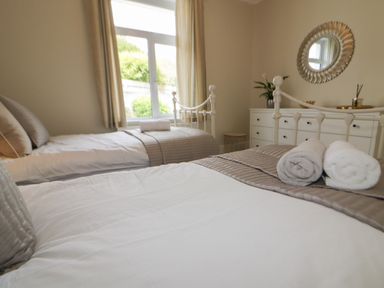 A bedroom with two single beds a window and a dresser with a round mirror at Robin Hill in Duporth near St Austell