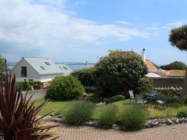 A garden with outdoor chairs and table surrounded by bushes and houses near the sea at Robin Hill in Duporth near St Austell