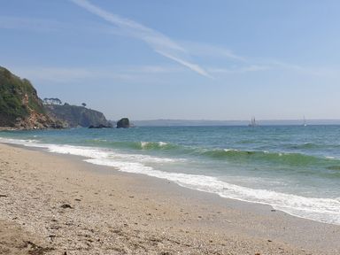 A sandy beach with waves rolling in and cliffs in the background at Robin Hill in Duporth near St Austell