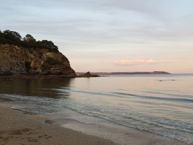 A coastal scene with a sandy beach a rocky cliff and calm sea under a cloudy sky at Robin Hill in Duporth near St Austell