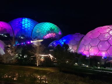 Geodesic domes illuminated with colorful lights at night surrounded by trees and pathways at Robin Hill in Duporth near St Austell