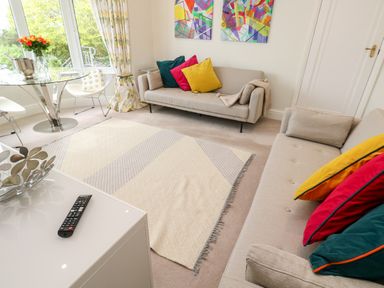 A living room with two sofas colorful cushions a rug a glass table with chairs and a bouquet of flowers at Robin Hill in Duporth near St Austell