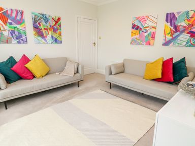 A living room with two beige sofas with multicolored cushions and abstract paintings on the walls at Robin Hill in Duporth near St Austell
